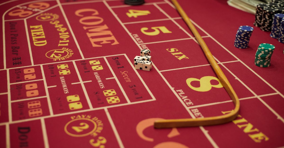 A red craps table contains dice, event chips, and a wooden stick arranged beside the numbered betting areas