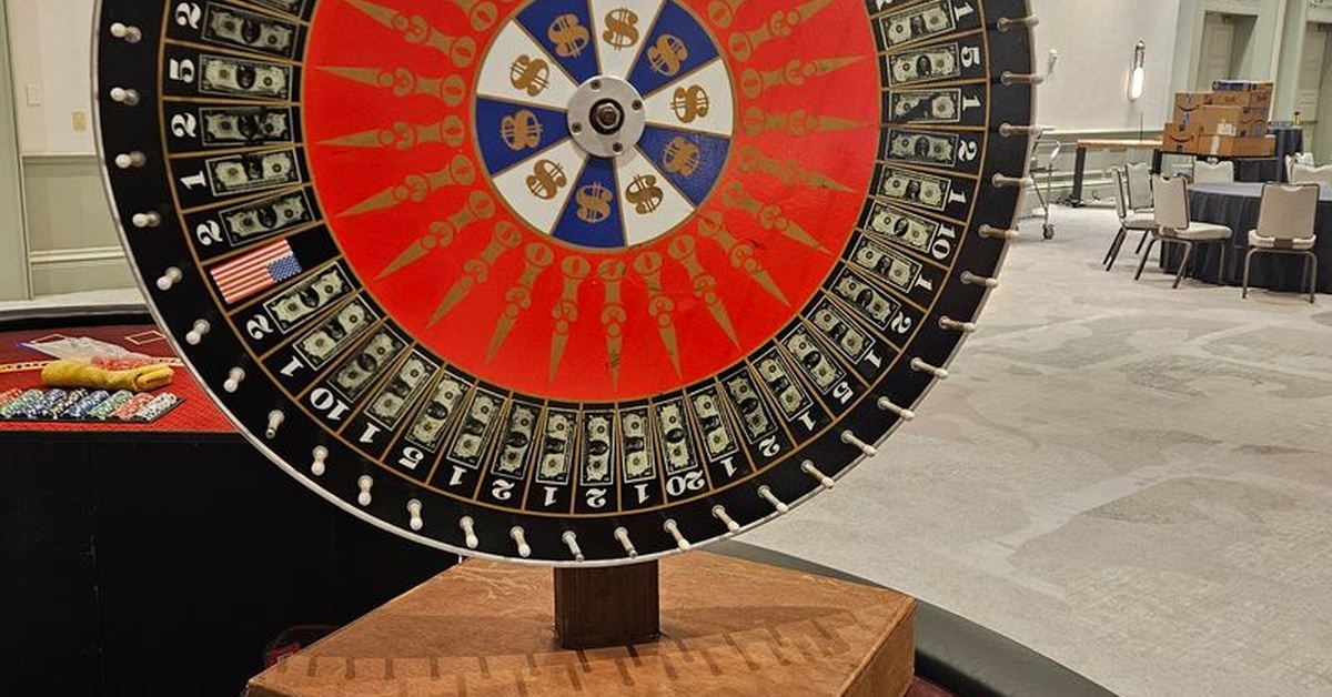 A large casino-themed prize wheel with dollar signs and numbered sections, surrounded by poker chips and gaming tables.