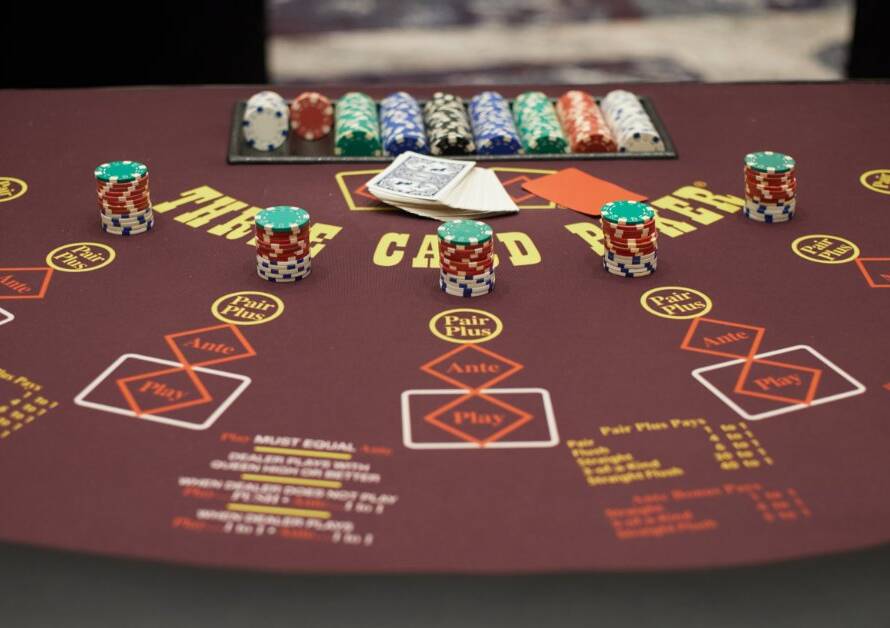 A burgundy poker table with stacks of casino chips, playing cards, and marked betting areas.