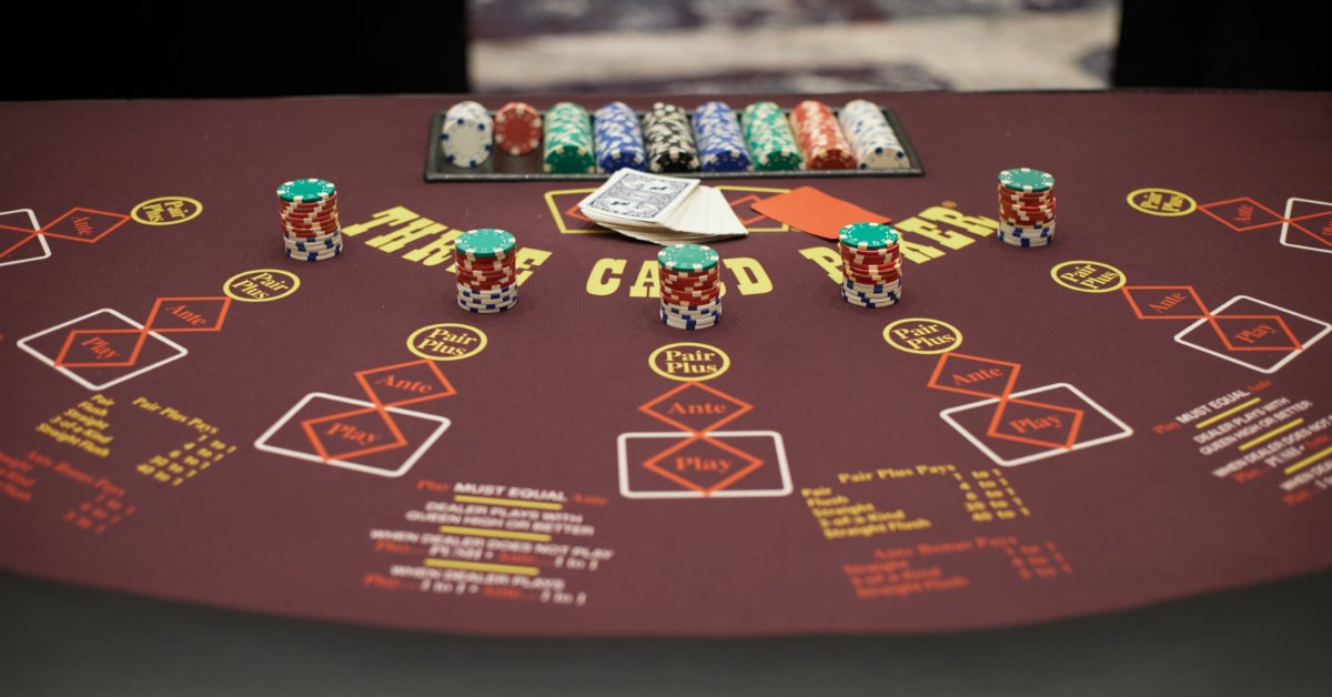 A burgundy poker table with stacks of casino chips, playing cards, and marked betting areas.