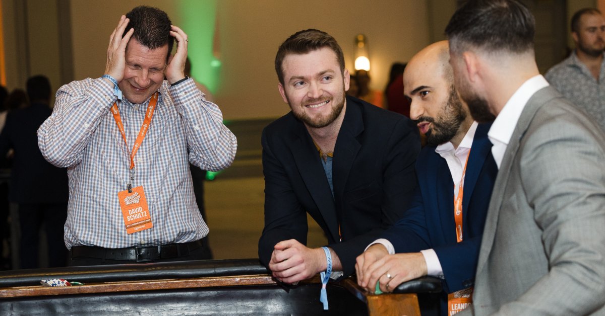 Four men gather around a casino table as one holds his head and the others smile and watch the game unfold.